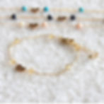 Gold bracelets with Scorpio zodiac symbol heart charms and citrine and other colorful beads on a soft, white textured surface