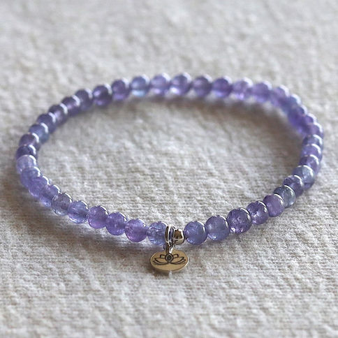 Tanzanite bead bracelet with a lotus charm on a beige textured surface. The atmosphere is calm and elegant.