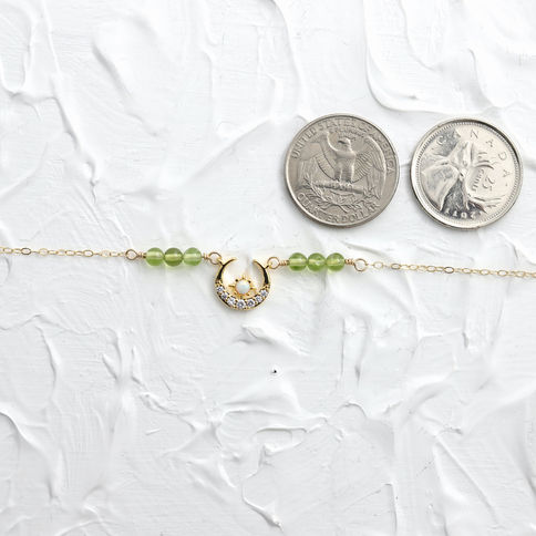 premium gold necklace with natural peridot beads and crescent moon charm next to quarters on a white surface.