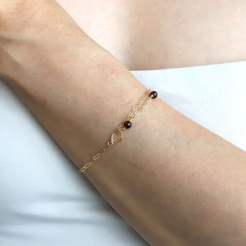 Close-up wearing a Garnet station and paperclip bracelet, hammered figure 8 charm, artisan unique layered birthstone jewelry.