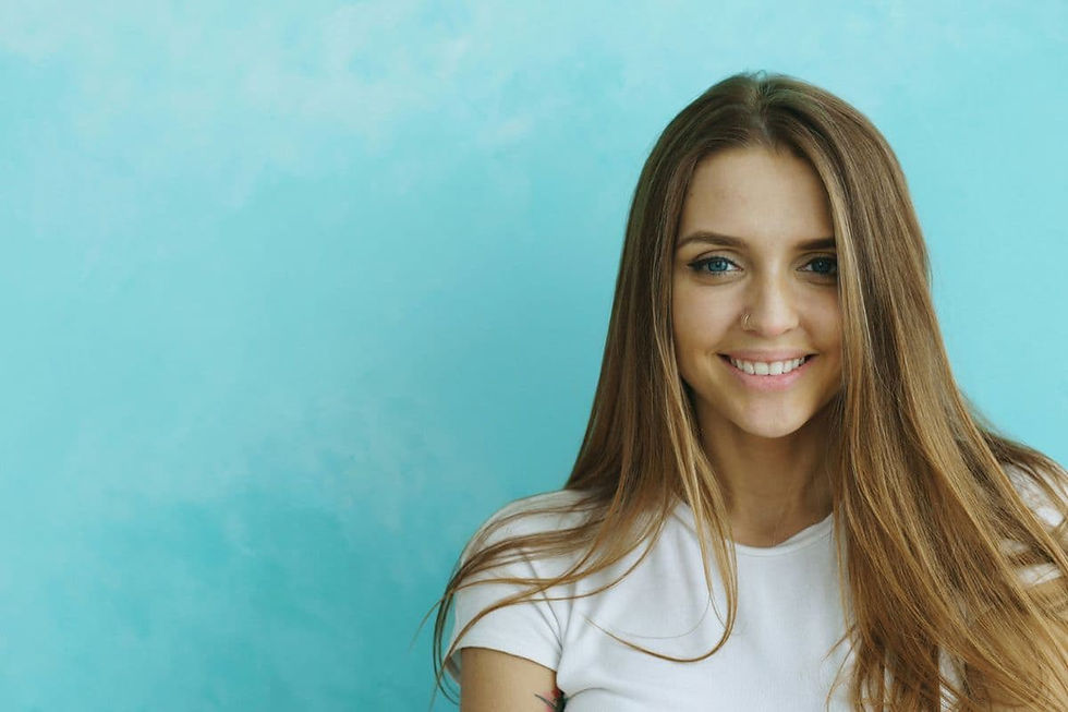 Smiling young woman with long brown hair in a white shirt against a turquoise background, featuring Water signs zodiac jewelry styling