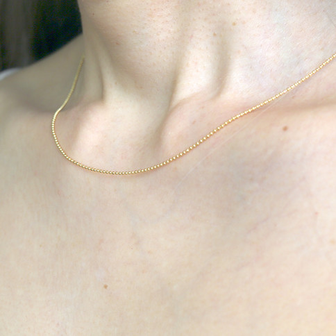 Close-up of a gold ball chain necklace. The background is neutral, highlighting the simplicity and elegance of