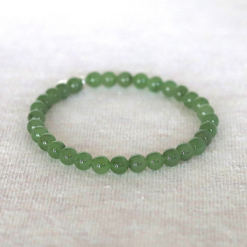 Green jade bead bracelet on a soft, light beige surface. The beads are glossy and evenly spaced, creating a simple, elegant l