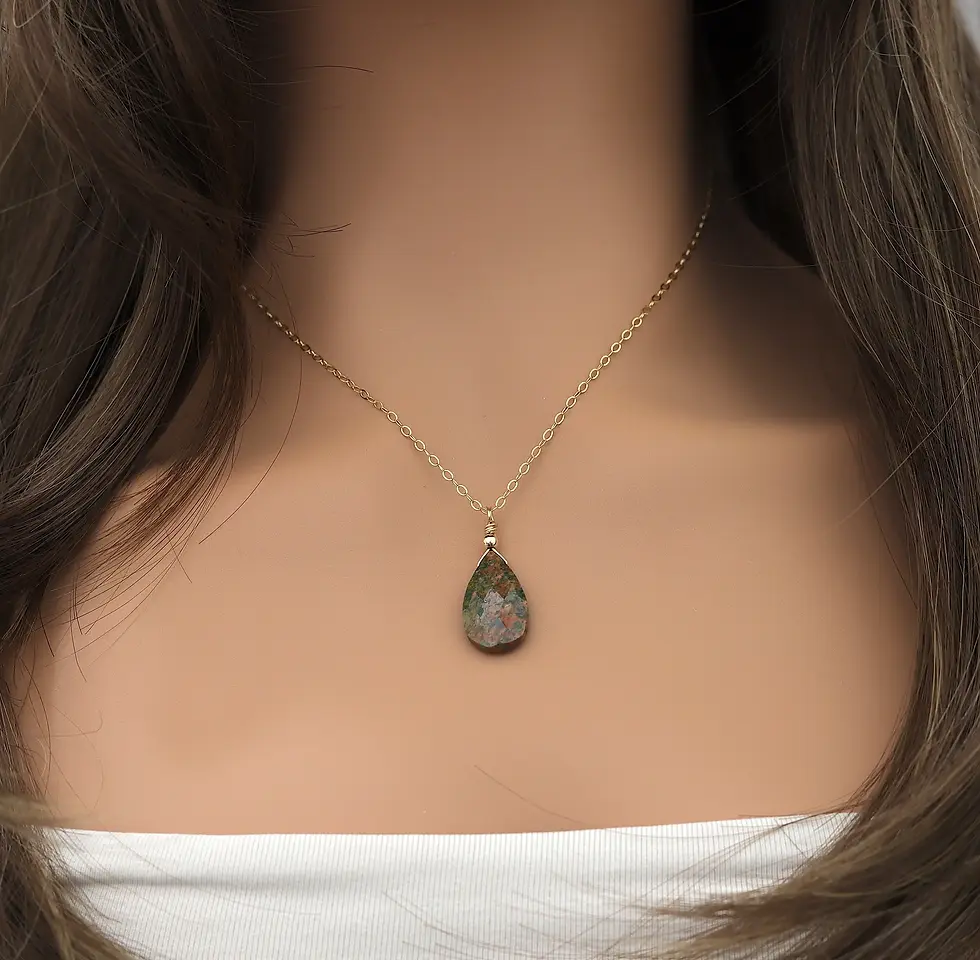 Gold chain with a teardrop unakite stone pendant on a woman's neck. She is wears a white top, creating a simple, elegant look