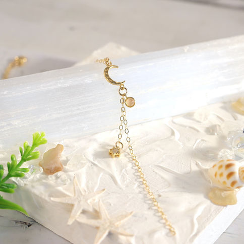 Moon and star lariat necklace with 14k gold chain. on white textured surface, Celestial and cosmic jewelry, Elegant mood.