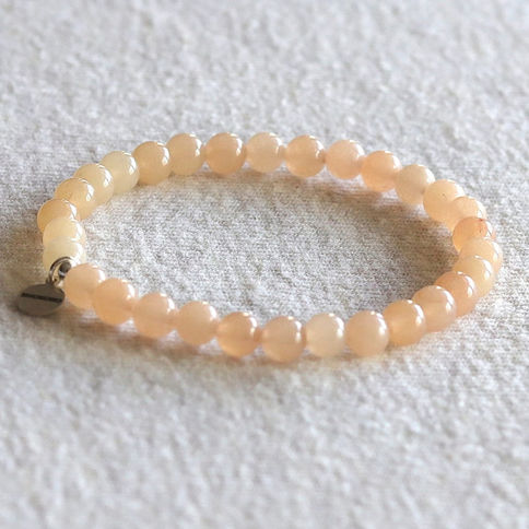 Peach pink aventurine bead bracelet with a small metal tag on a textured white surface, conveying a minimalist and elegant.