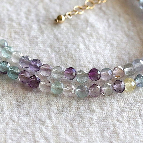 Close-up of a rainbow fluorite beaded necklace with faceted gemstones on a soft, with 14k gold filled clasp.