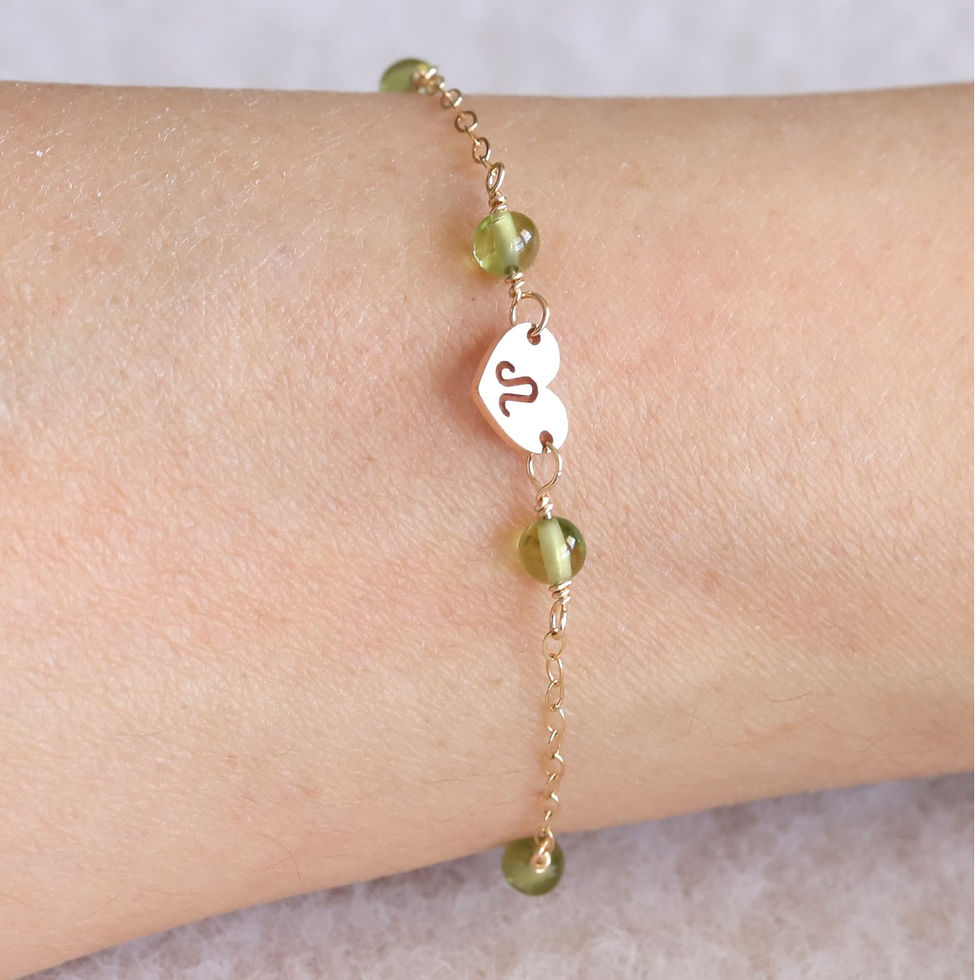 Zodiac Leo symbol heart charm with delicate gold chain and green peridot beads on wrist. Soft background enhances elegance.