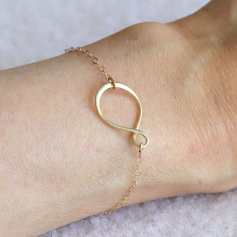 A woman wearing a dainty 14k gold-filled infinity bracelet styled for a minimalist, everyday look.