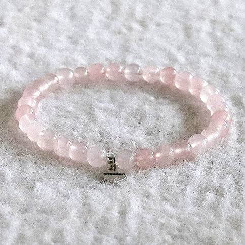 Pink calcite bead bracelet on a textured white background. A small metallic tag is attached, creating an elegant and serene.