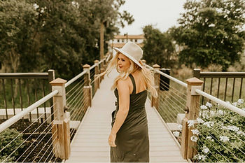 Blonde woman in a black dress and white hat looks back, a perfect fashion guide for wearing Taurus zodiac jewelry.