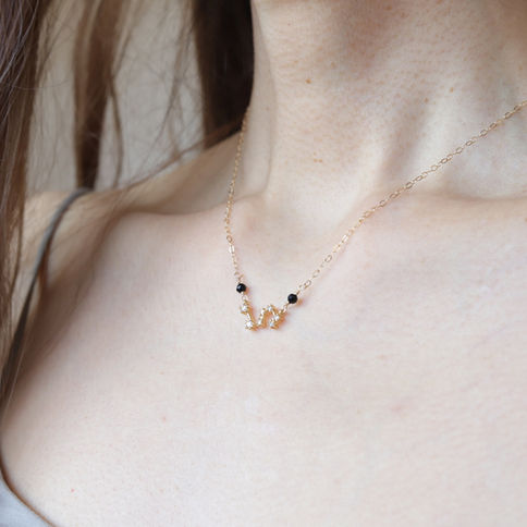 Close-up of a woman's neck wearing a gold Leo zodiac constellation necklace with birthstones, neutral background.