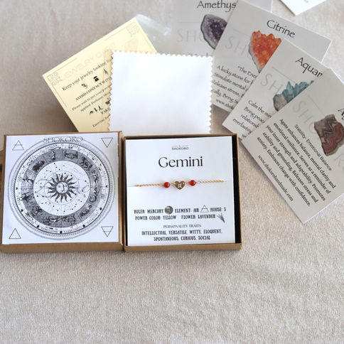 Gemini bracelet with red gemstone beads in a box, zodiac chart, crystal cards. Beige background, cosmic and mystical theme.