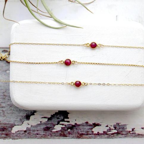 Gold bracelets with red ruby stones displayed on a white block, white and gray wooden surface, Elegant and feminine jewelry