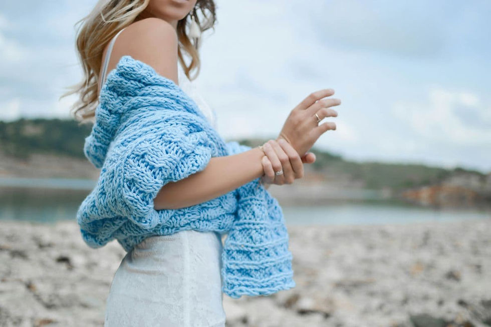 A woman in a white dress with a blue knitted shawl stands by a rocky lakeside. featuring the complete styling guide look with Shokoro Handmade Aquamarine jewelry