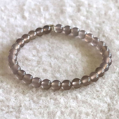 Purple chalcedony bead bracelet on a textured light surface. Beads are glossy and evenly spaced, creating a circular shape. S