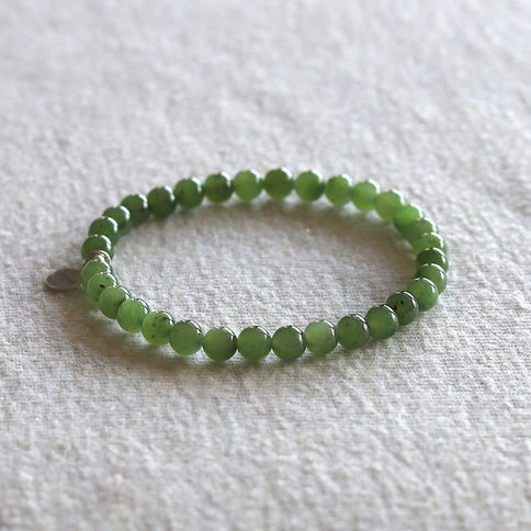 Natural green jade bead bracelet on beige fabric background, displaying a simple and elegant design.