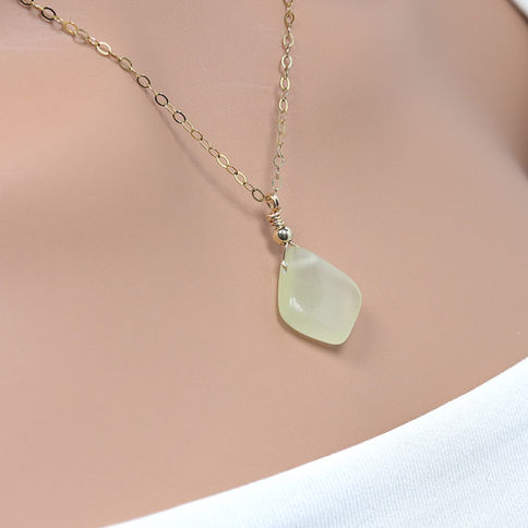 Gold chain necklace with a pale yellow calcite pendant on beige skin. showcasing the jewelry's elegant simplicity.