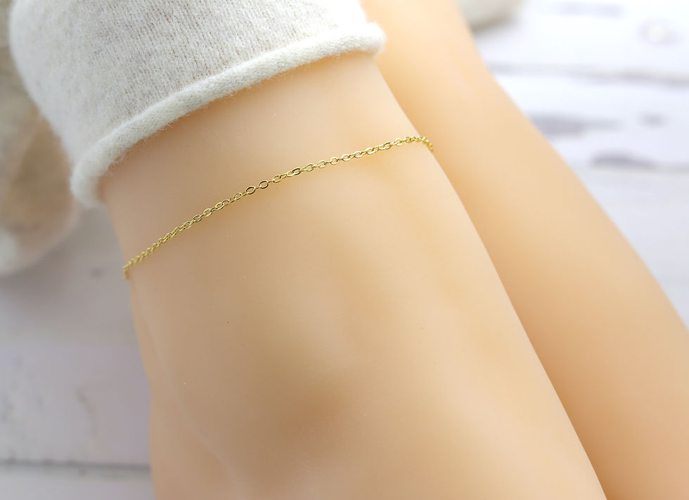Gold anklet on a smooth leg with a white fuzzy sock. Soft lighting and a blurred white background create a serene atmosphere.