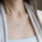 A woman wears a gold Taurus symbol and heart-shaped necklace with small design. She's dressed in a white top and cardigan. Soft light creates a gentle mood.