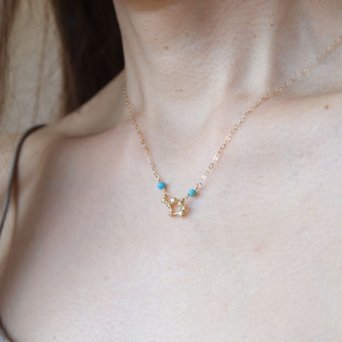 A delicate sagittarius gold necklace with real turquoise and a charm is worn around a woman's neck, Celestial and star sign j