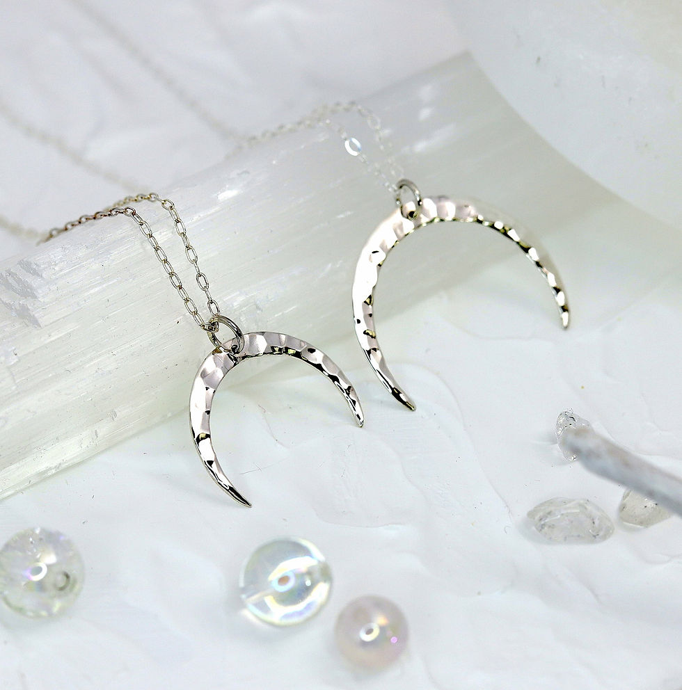 Silver hammered crescent moon necklaces on white textured surface, surrounded by translucent beads, creating a calm, elegant