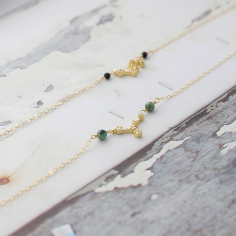 Cancer zodiac gold necklaces with real emerald lie on a textured, Elegant, rustic mood. Cosmic and symbolic jewelry.