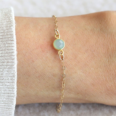 A delicate gold chain bracelet with a blue chalcedony gemstone on a wrist. The background is soft and neutral. minimalistic.