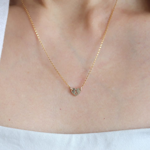 Gold necklace with heart pendant featuring Capricorn zodiac sign, wearing a white top. Soft, minimal background.