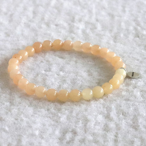 Pink aventurine bracelet with a silver tag rests on a textured white surface, creating a calm, minimalist vibe.