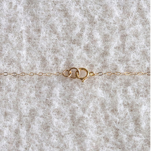 Gold chain necklace with small links and clasp on a soft, textured beige fabric background. The setting is calm and elegant.
