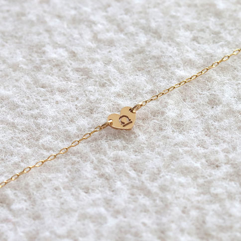 Gold anklet with heart charm featuring a Libra symbol on textured white fabric backdrop, evoking a sense of elegance.