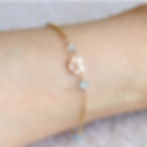 A gold bracelet with a heart charm and Aquarius zodiac symbol on a wrist. Blue aquamarine beads are interspersed.