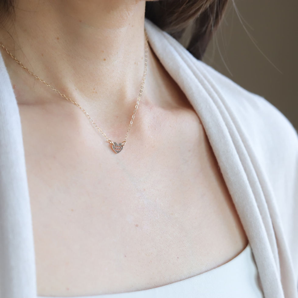 Close-up of a person wearing a gold heart-shaped Aquarius sign necklace. They are dressed in a light beige top. Serene mood