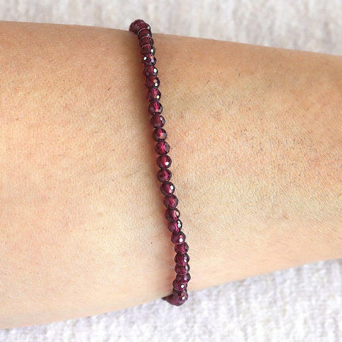 A wrist with a delicate garnet beaded bracelet on skin. The beads are small and reflective. The background is a soft.