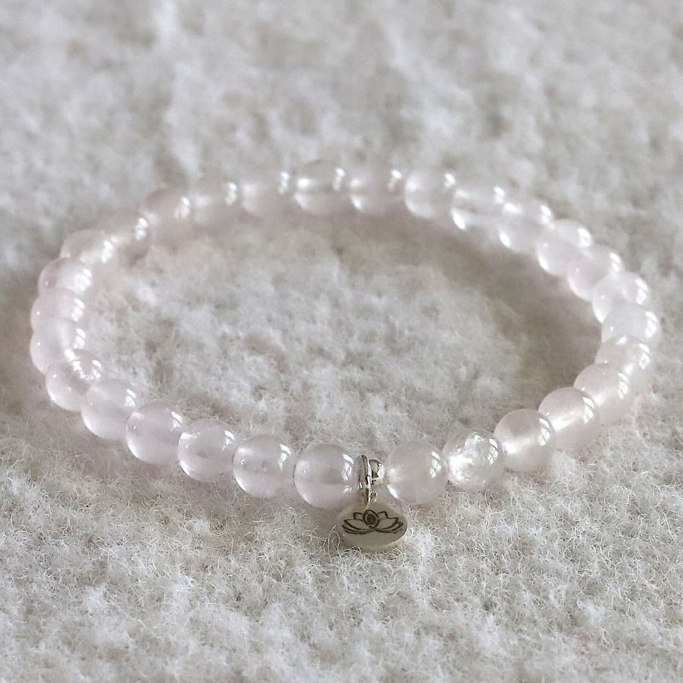 Rose quartz bead bracelet with a lotus charm, resting on a soft, textured white surface. The mood is serene and calming.