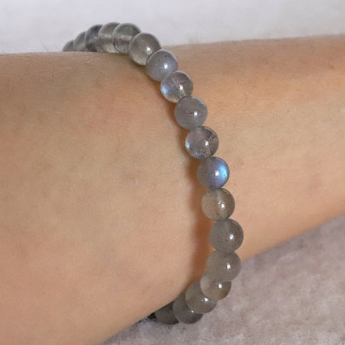 Gray labradorite bead bracelet on wrist, glowing blue hues. Soft, neutral background creates a calm, stylish mood.