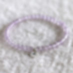 Purple lavender amethyst bead bracelet with lotus charm on a fluffy white surface. The translucent beads create a calm and pe