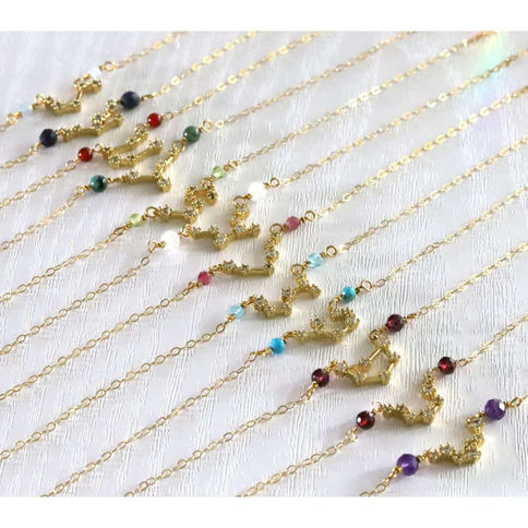 Angled phot of 12 personalized gold-filled zodiac constellation necklaces with natural birthstones, artisan custom gift.