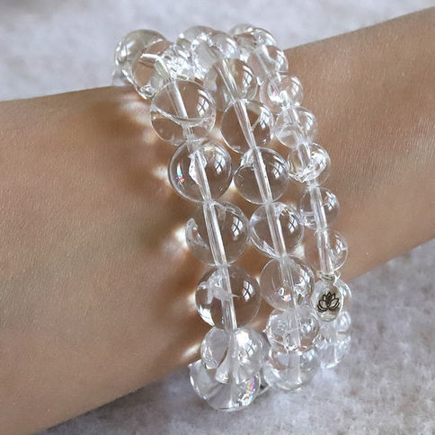 Samadhi clear beaded bracelet with a lotus charm on wrist, against a soft textured background. Reflective surfaces.