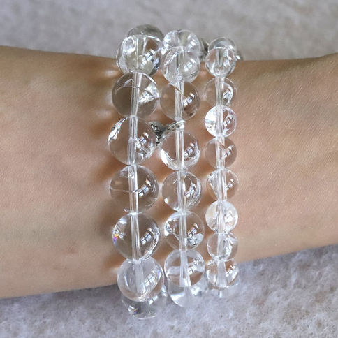 Himalayan quartz beads form three bracelets on a wrist against a soft, light gray background. The beads reflect light.