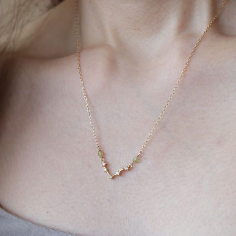 A close-up of a person wearing a Libra constellation necklace with peridot gems on a light skin backdrop, Minimalist jewelry.