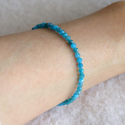 Hand wearing a blue apatite beaded bracelet on a textured background. The beads are small and shiny, creating a calm mood.