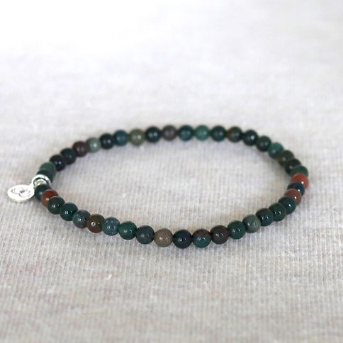 Bloodstone bead bracelet with mix stones and a silver charm on a textured light gray surface. Minimalistic and elegant design