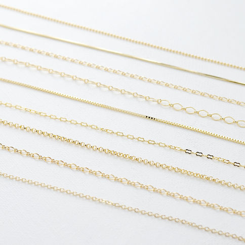 Various gold chains with different link patterns arranged on a white textured surface, showcasing elegant designs and subtle