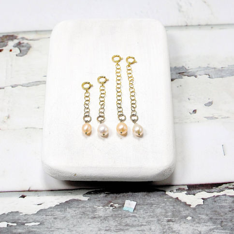 Three pearl charm necklace extenders with 14k gold filled chains on a wooden display against a rustic, Elegant design.