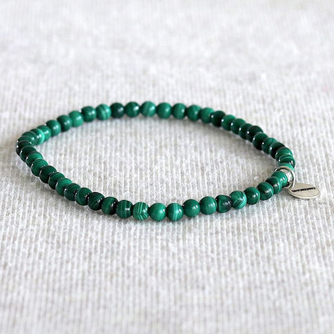 Malachite beaded bracelet on a textured light gray surface. The bracelet features round, glossy beads with subtle stripes,