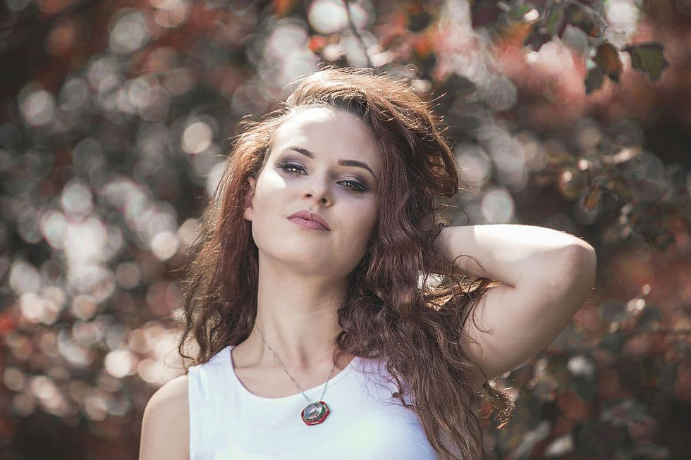 Portrait of a woman in a white top, hand behind her head, wearing a Clear Quartz necklace, 