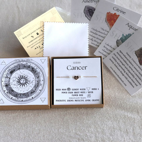 Cancer zodiac gold bracelet on display with astrology cards for birthstones. Beige background, detailed text visible.