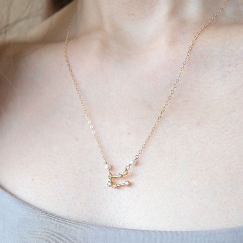 Gemini zodiac gold necklace with a constellation pendant with pearls on a person's neck, wearing a gray top. Symbolic jewelry